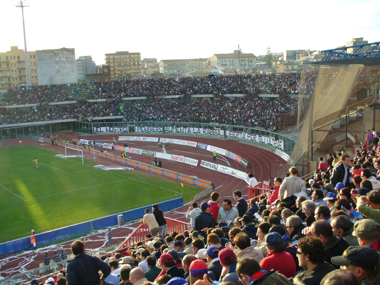 Panoramica del campo di gioco in erba sintetica e delle tribune del Campo Comunale di Nesima — Licenza: Creative Commons CC BY-SA 4.0 — Crediti: Archivio Storico Calcio Catania